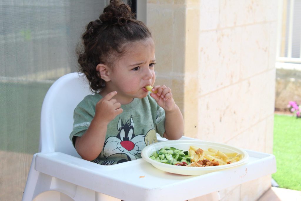 Kind sitzt auf Hochstuhl und isst